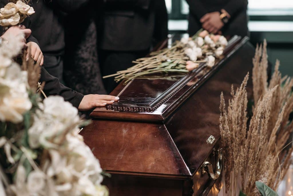 A woman’s hand on a coffin surrounded by flowers.